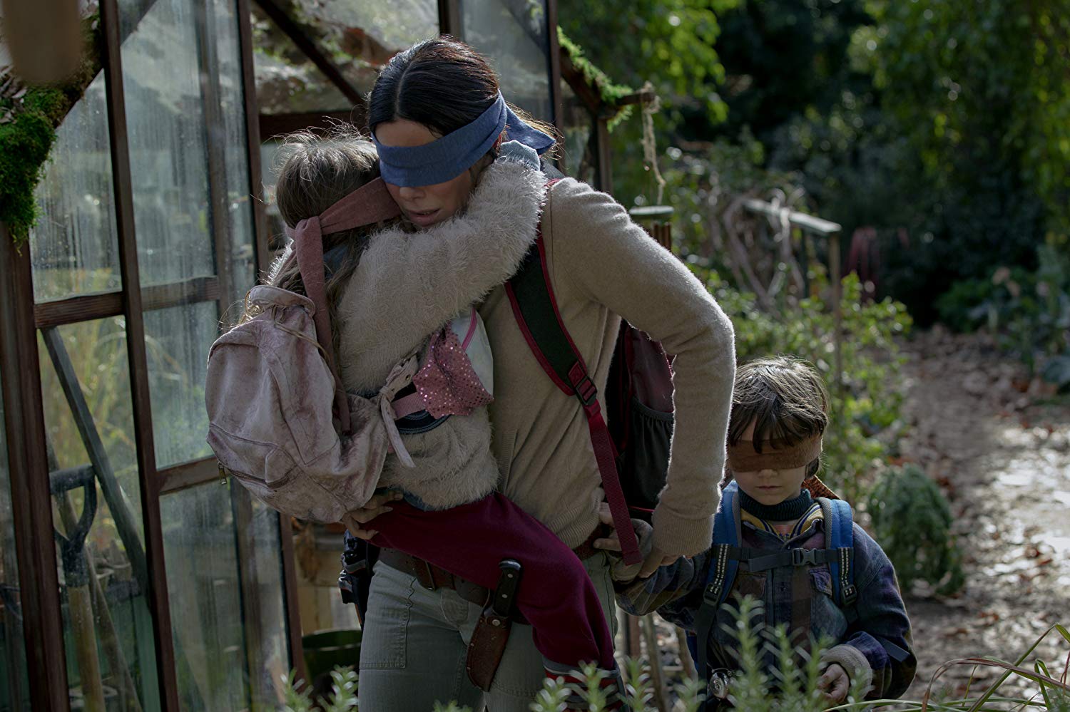 Movie still from Bird Box showing Sandra Bullock with a boy and a girl, all wearing blindfolds.